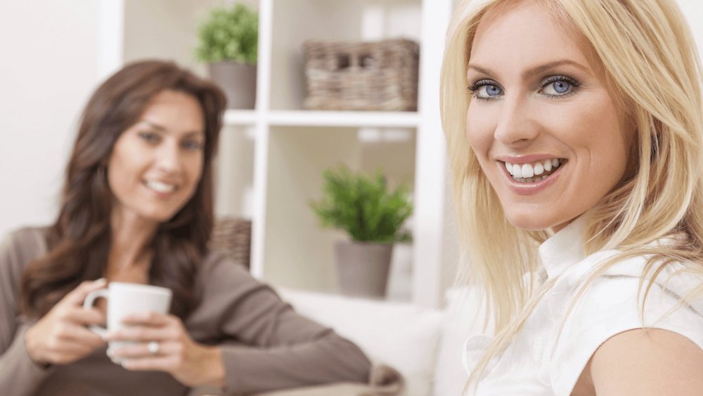 Blonde woman smiling with a woman in the background is blurry